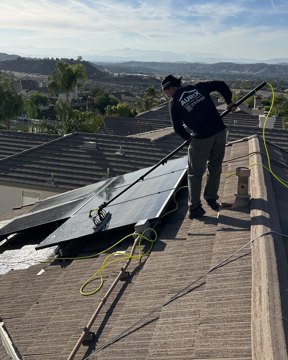 An Aurix technician cleaning a residential solar array with a water-fed pole